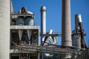 Close-up of a large industrial factory with concrete chimneys and metallic pipes against a clear blue sky.